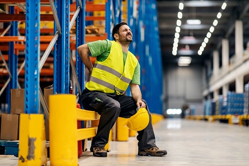 Warehouse worker in a reflective vest touching his back