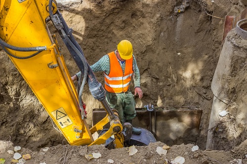 Construction worker in a trench next to an excavator boom