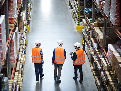 Workers in helmets and vests walking through a warehouse.