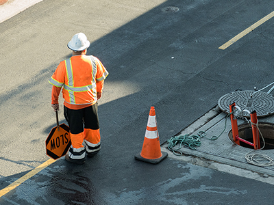 Worker wearing an orange safety vest and hard hat in a higway work zone.